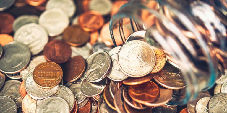 Coins scattered on a surface, with some spilling out of a glass jar.