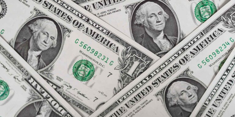 Multiple one-dollar bills featuring George Washington's portrait, arranged in a scattered layout.