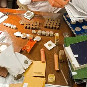 Numerous coins and coin-related materials are spread across a table