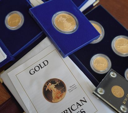 Gold coins displayed in blue cases alongside a booklet titled "GOLD AMERICAN EAGLES."