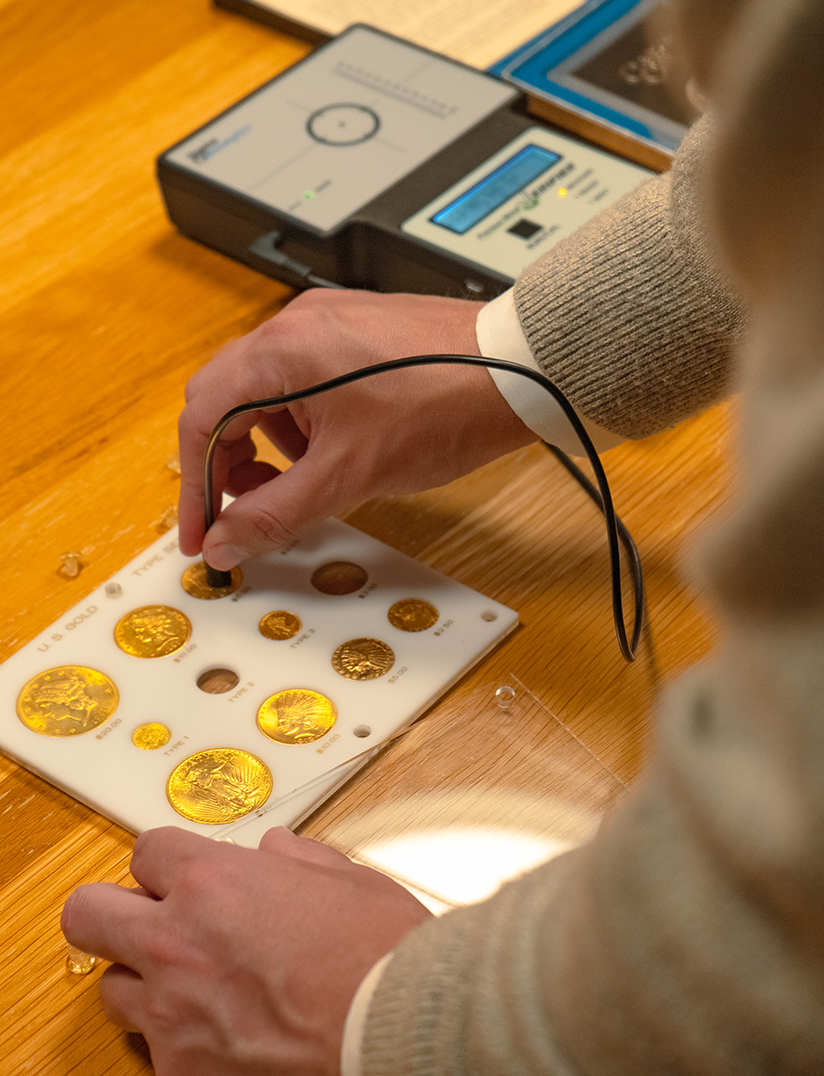 Expert examining gold coins with a testing device.