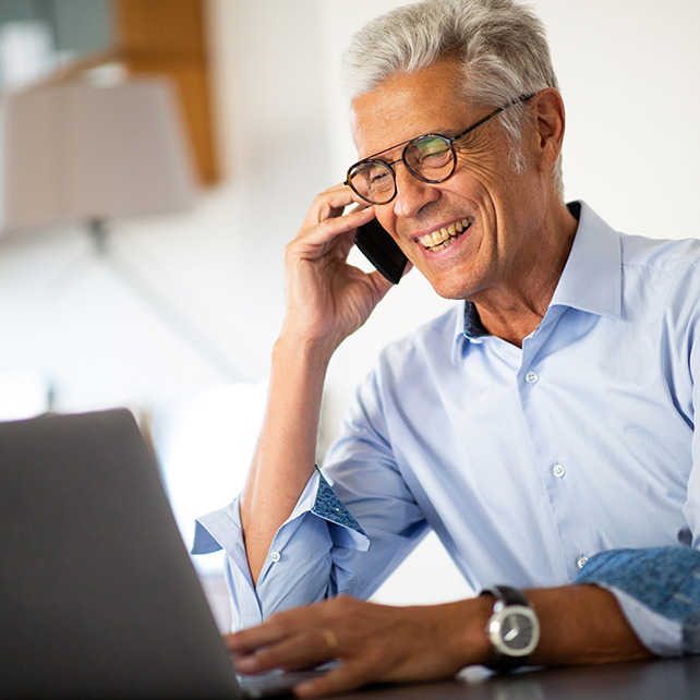 Close up portrait smiling businessman talking with phone while looking at laptop computer