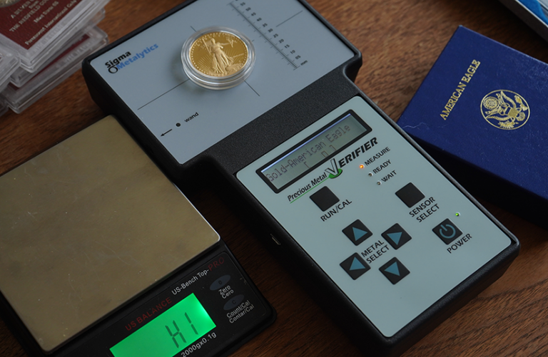 Gold coin on a metal verifier device, with a scale and a blue booklet labeled "American Eagle."