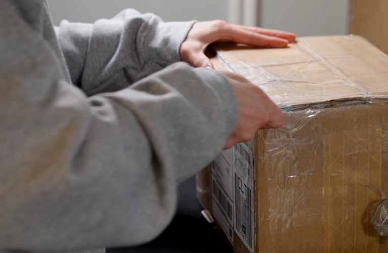 Opening a sealed cardboard box with hands, revealing contents inside.